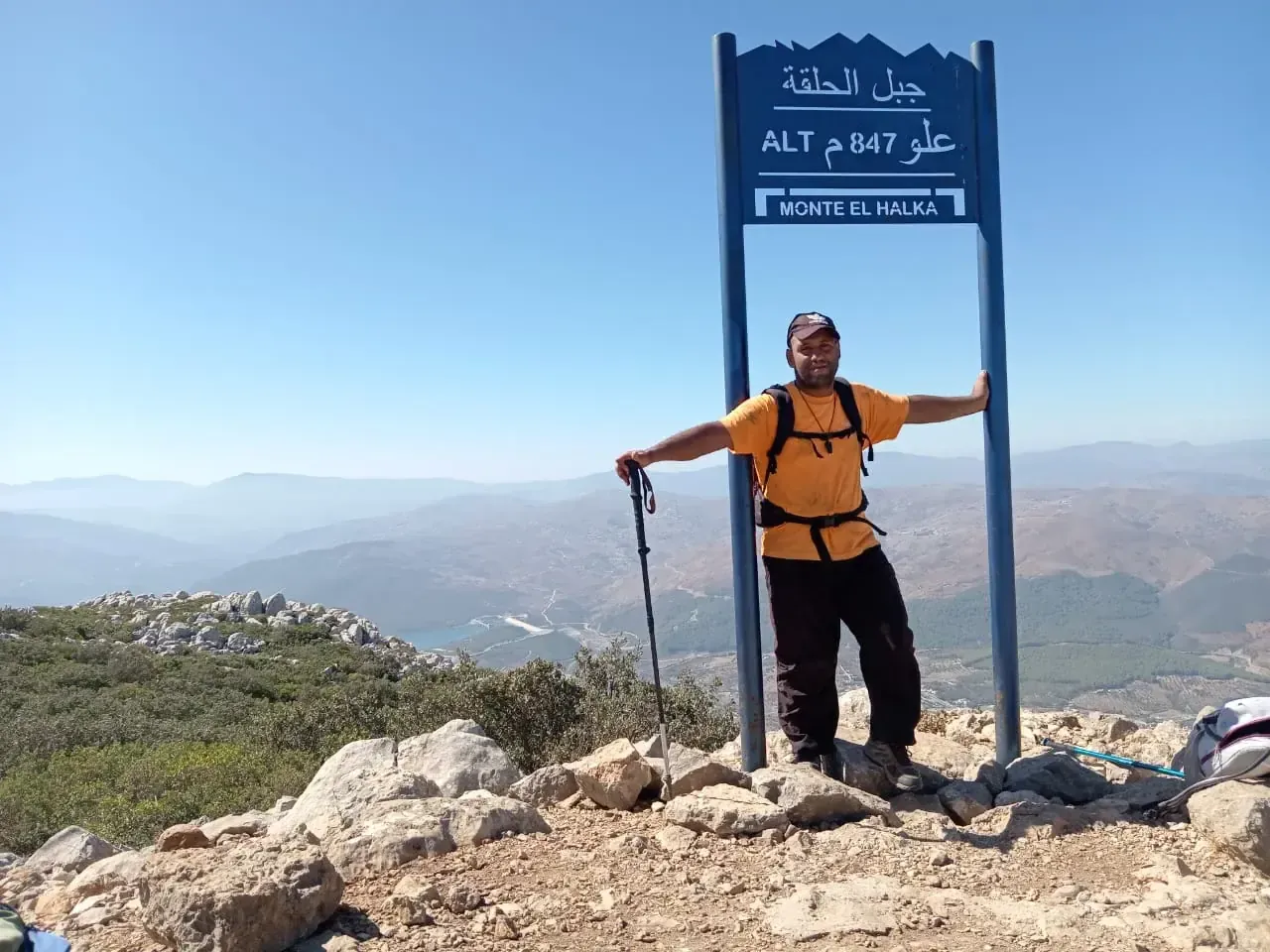Guide Imad Ben Yahya between the posts of the Jbel El Halqa summit sign, with mountain ranges behind