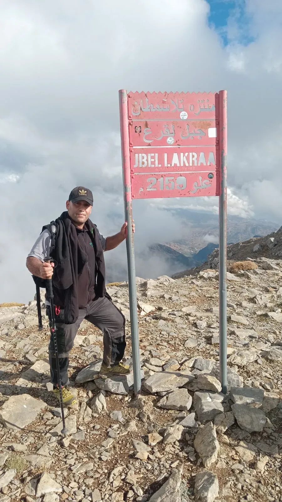 The red summit sign of Jbel Lakraa on the summit rocks, with guide Imad Ben Yahya